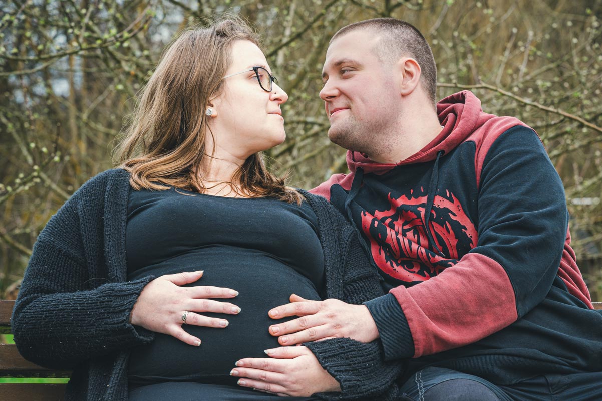 Eine schwangere Frau blickt ihren Mann in die Augen. Beide berühren mit den Händen den Babybauch.