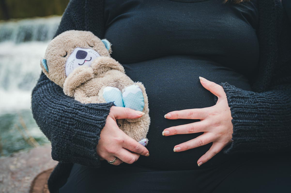 Ein junge schwangere Frau fühlt ihr ungeborenes Baby am Bauch und hält einen Teddy im Arm