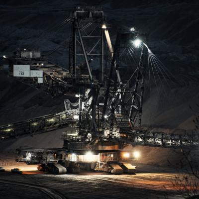 Ein Kohleradbagger von Terra Nova verrichtet in den abendlichen Stunden seine Arbeit. Viele Scheinwerfer leuchten den Arbeitsbereich aus.