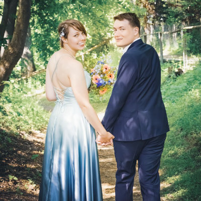 Das Brautpaar geht Hand in Hand vom Fotografen weg und blickt lächelnd über die Schulter zurück.